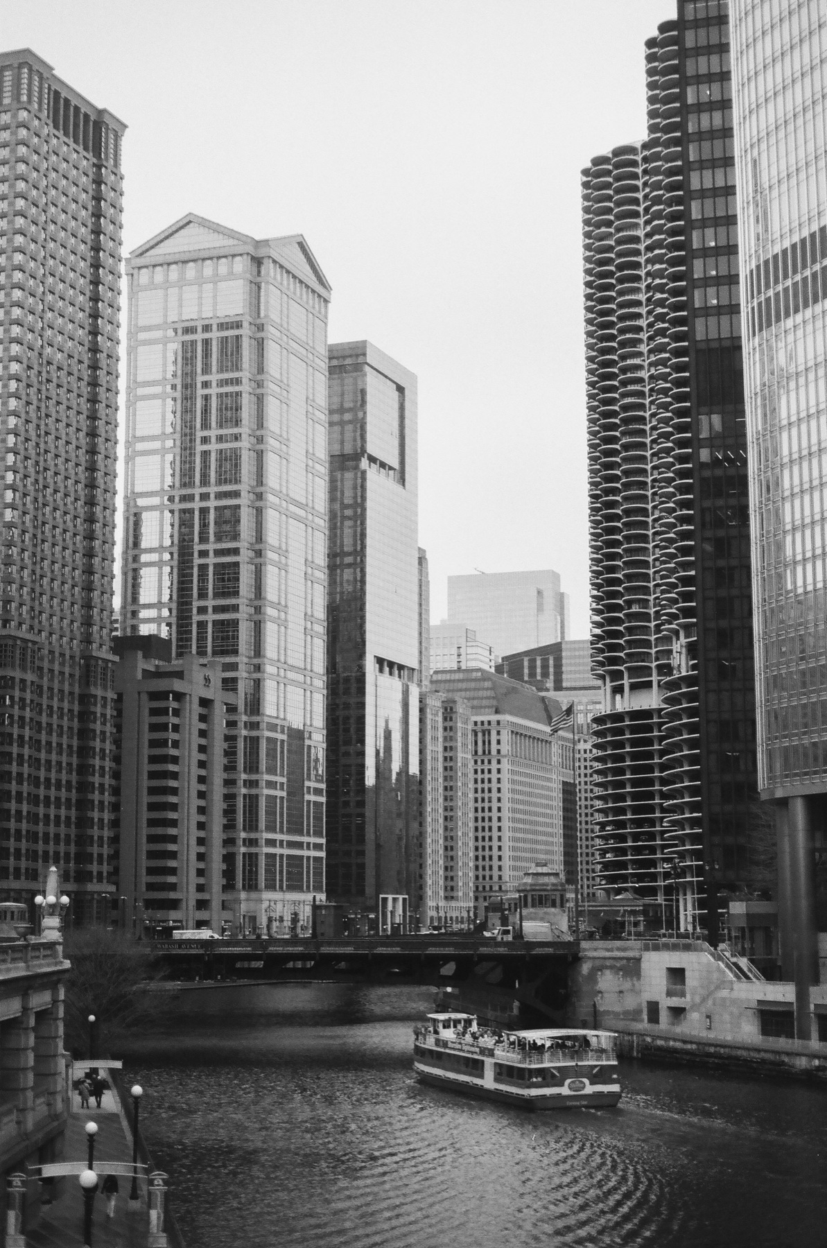 Black and white view of the Chicago River between skyscrapers with a tour boat